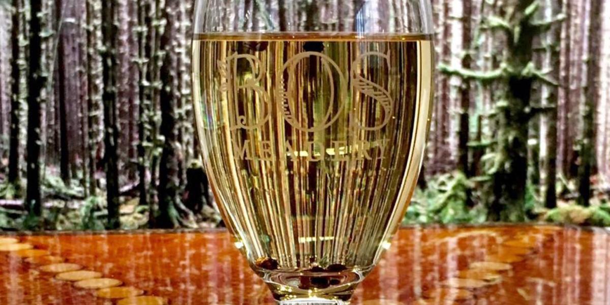 A glass of mead with the Bos Meadery logo
