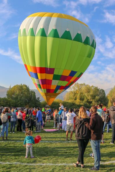 A little girl with balloon in a crowd looking at a large hot air balloon