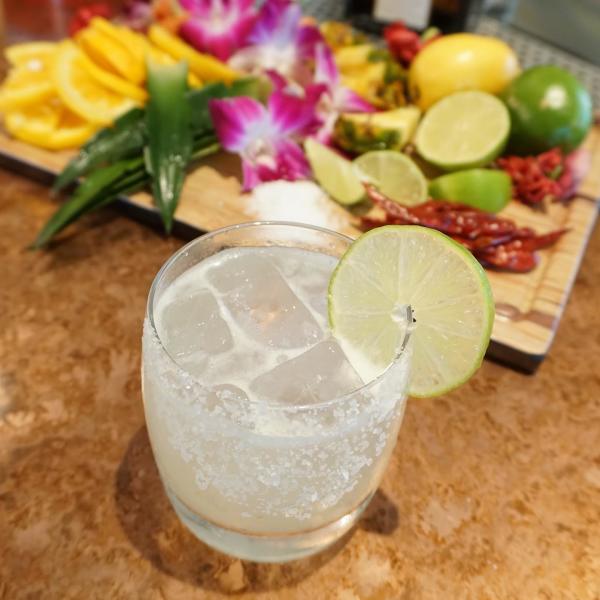 A fresh cocktail from Mexican Sugar sits against a backdrop of colorful fruits and flowers.
