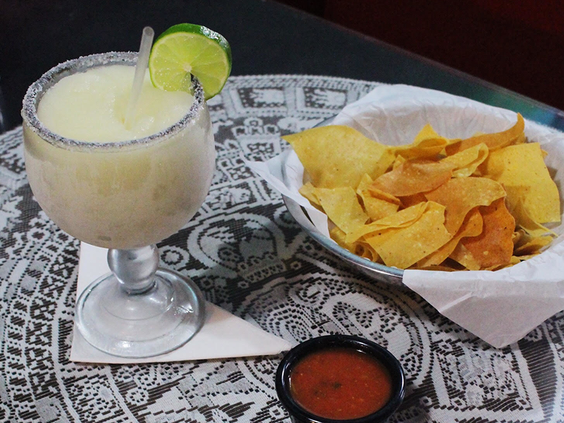 A frozen margarita from Arturo's is served in a salted glass with lime and fresh tortilla chips.