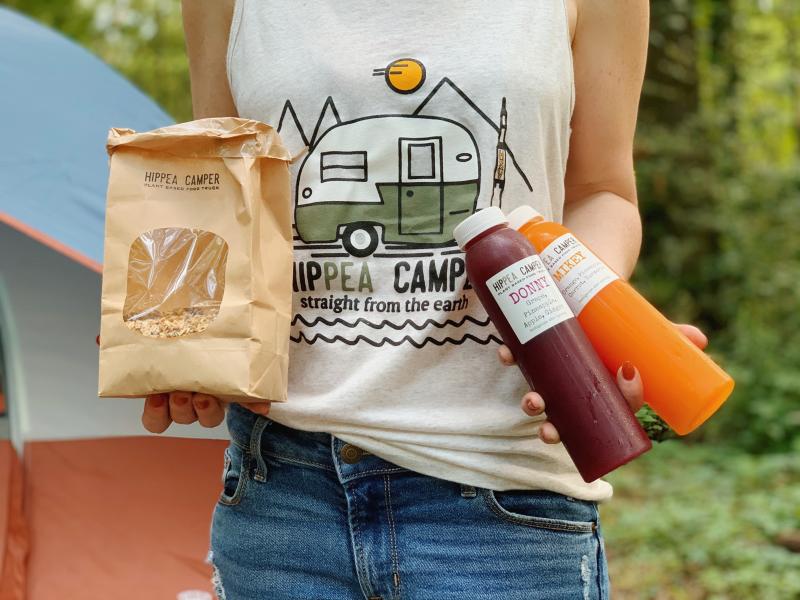 A woman holding food and bottles of juice from Hippea Camper Vegan food truck in Huntsville, AL