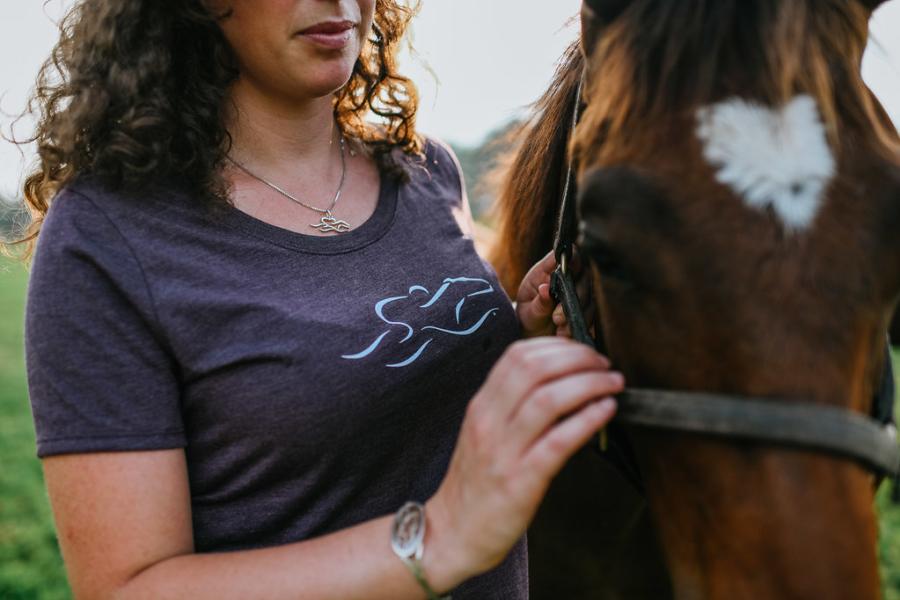 Woman wearing EMBRACE THE RACE jewelry and shirt with her horse