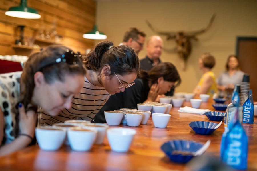 Photo of coffee lovers lean over coffee at Texas Coffee School during a cupping (tasting)