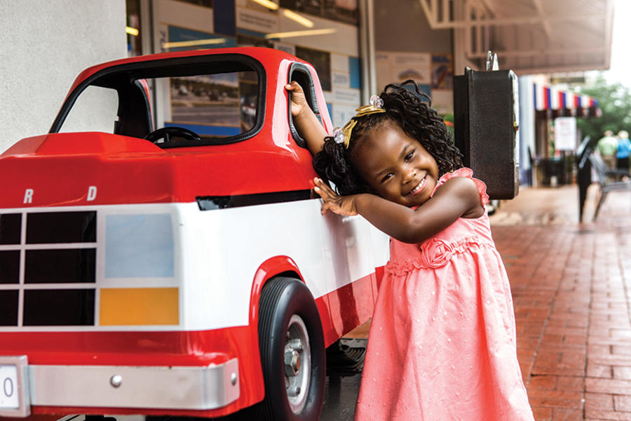 Image of a happy young girl leaning against a a coin operated replica of Sam Walton's truck