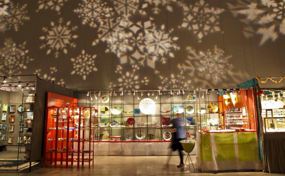 A vendor at the Armadillo Christmas Bazaar in front of a backdrop of snowflakes
