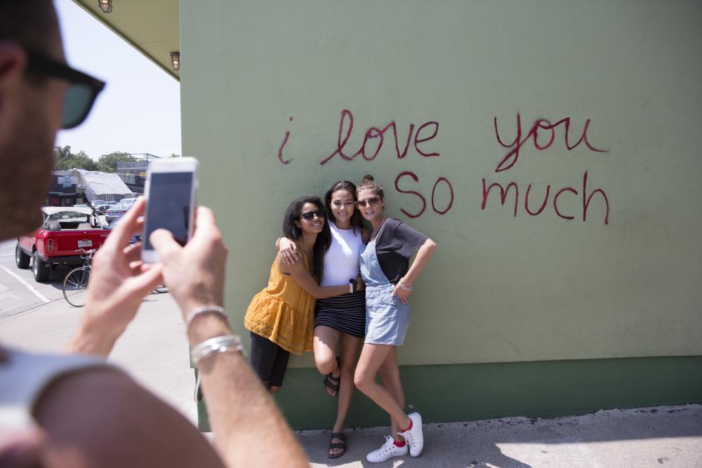 Girls posing at I Love You So Much Mural while friend takes photo