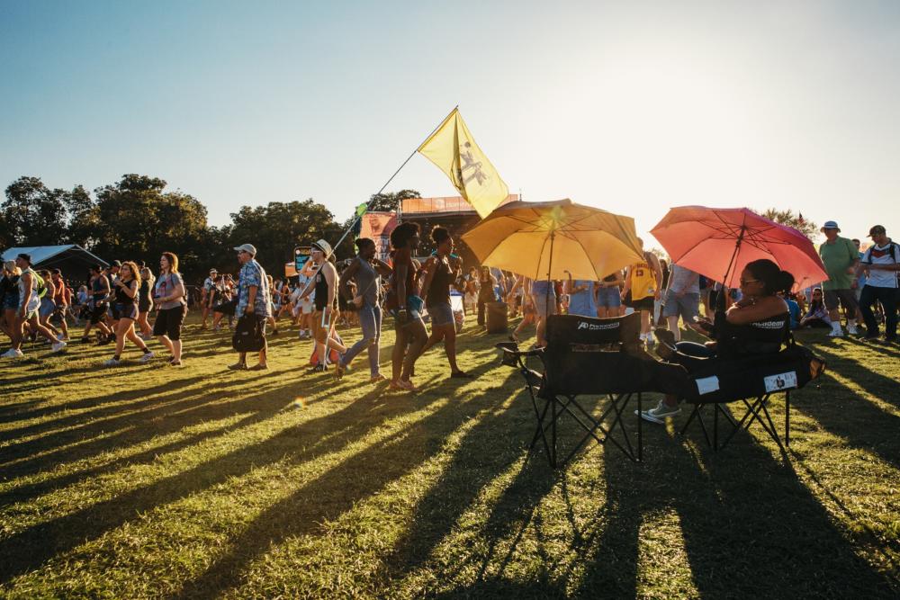 people in lawn chairs with umbrellas while crowd passes stage at ACL music festival in austin texas