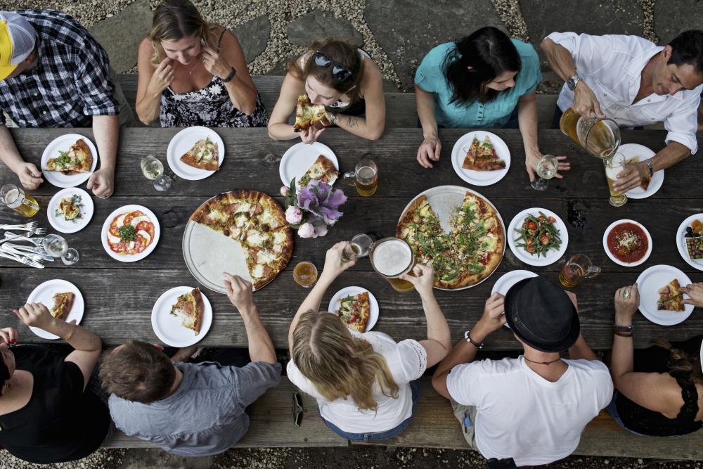 people dining with pizza and beer at large table