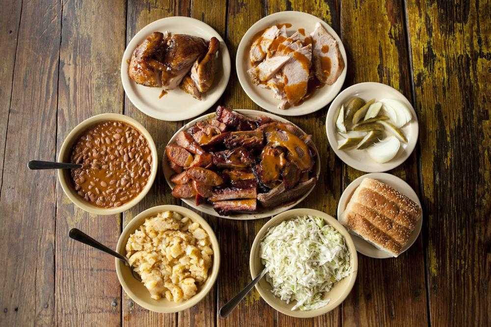 The Salt Lick barbecue staples with bowls of smoked meats beans potatoes cole slaw bread pickles and onions