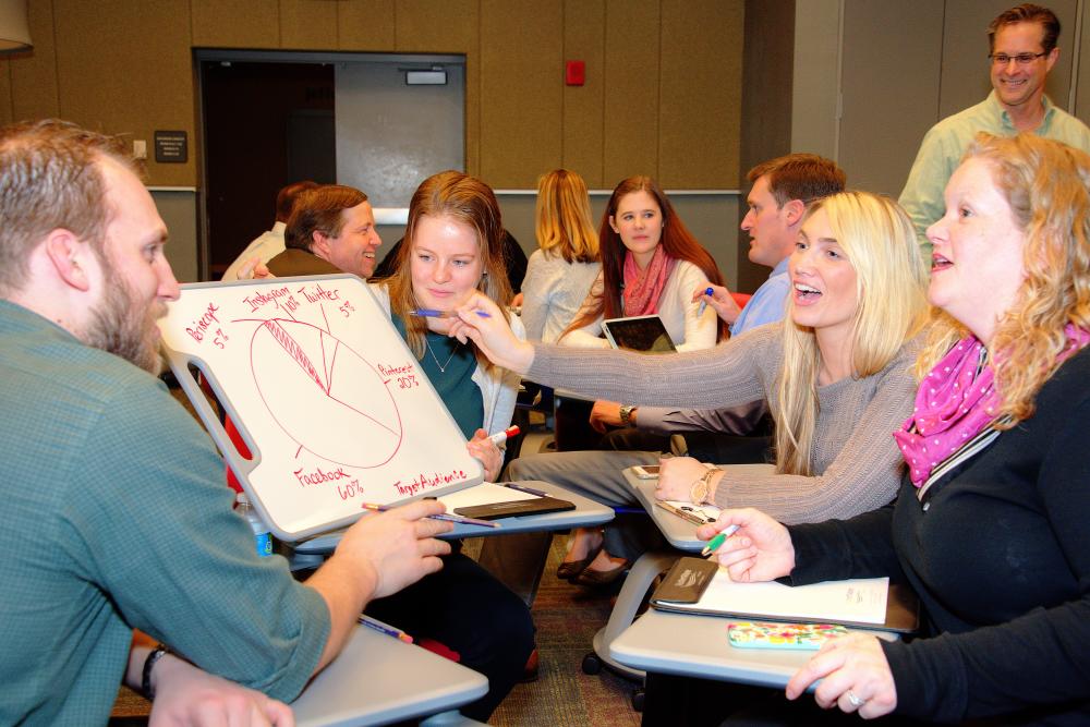 A group discusses a project while seated in movable desk chairs