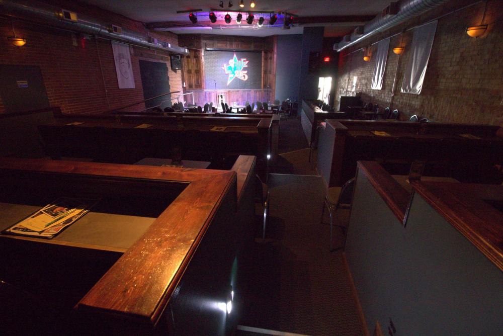 Inside the Loony Bin, a small comedy club with brick walls and tiered tabletop seating