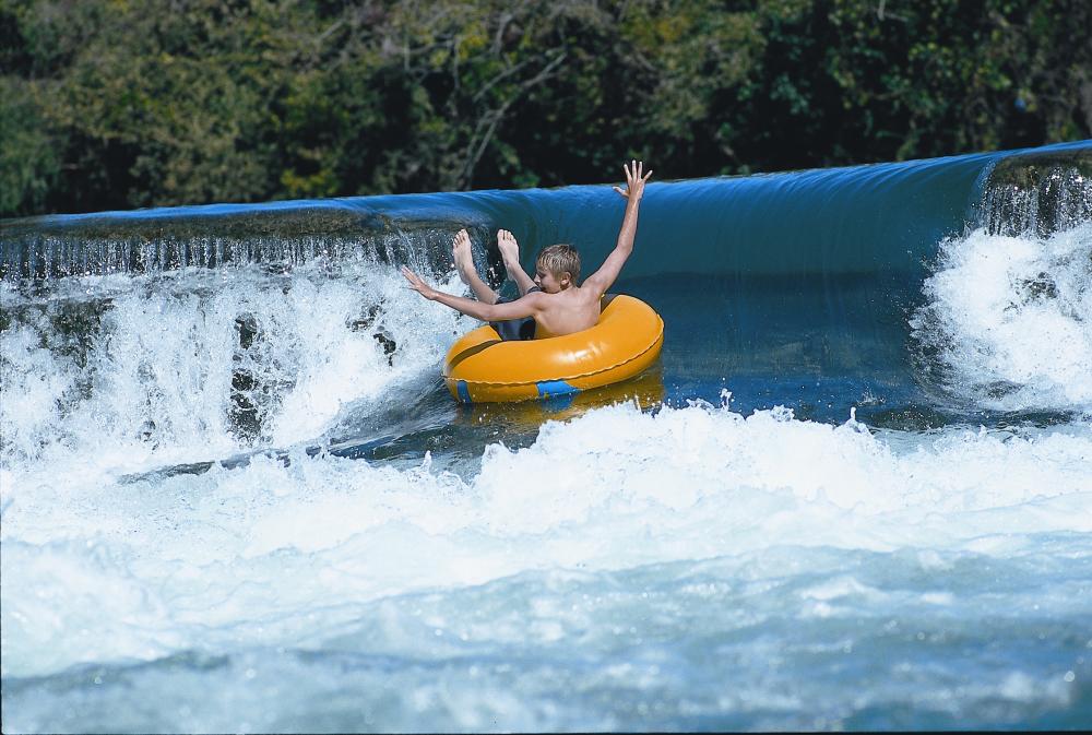 child waves arms in innertube on waterfall in San Marcos Texas