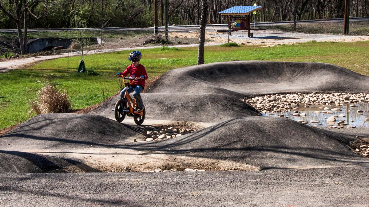 Boy on a bicycle with a helmet on the Mini bicycle pump track and kids loop trail