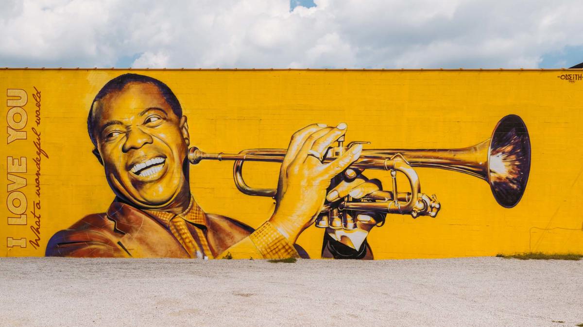 Photorealistic, bright yellow mural of Louis Armstrong smiling and holding his trumpet up to play. The words "I love you" and "What a wonderful world" are painted on the left hand side of the mural.