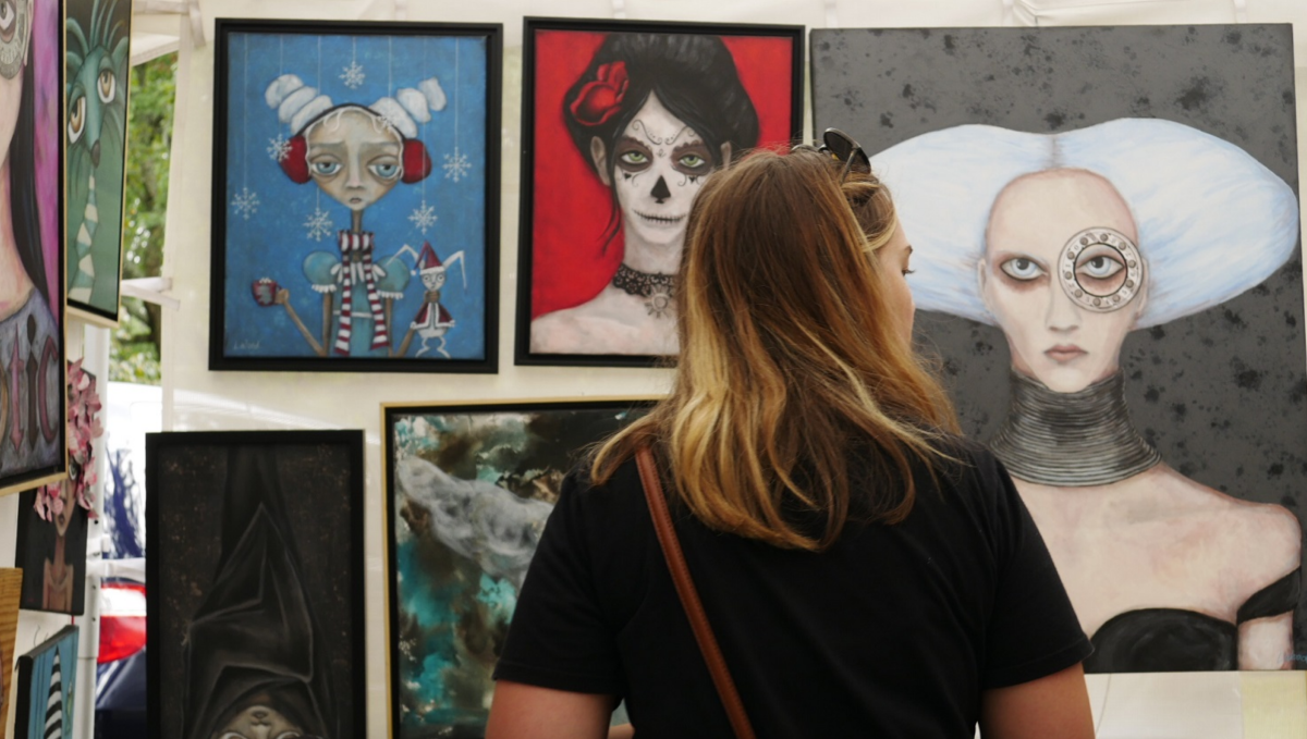 A woman stands in front of a tent filled with paintings at the Monte Sano Art Festival in Huntsville, Alabama