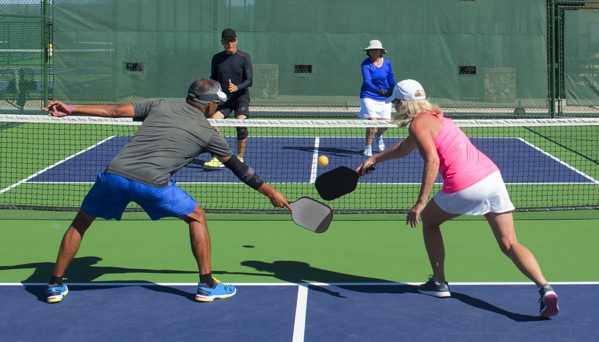 2 couples playing pickle ball on an outdoor court