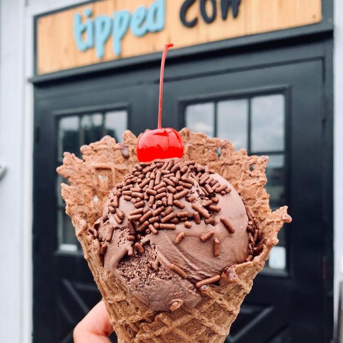 Chocolate ice cream in a waffle cone with sprinkles and a cherry on top from Tipped Cow Creamery