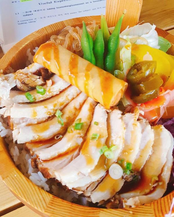 bowl of food with chicken, vegetables and an egg roll