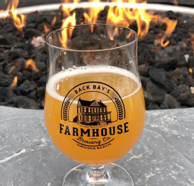 A glass of cider Back Bay Farmhouse Brewing sits next to a warm fire pit.