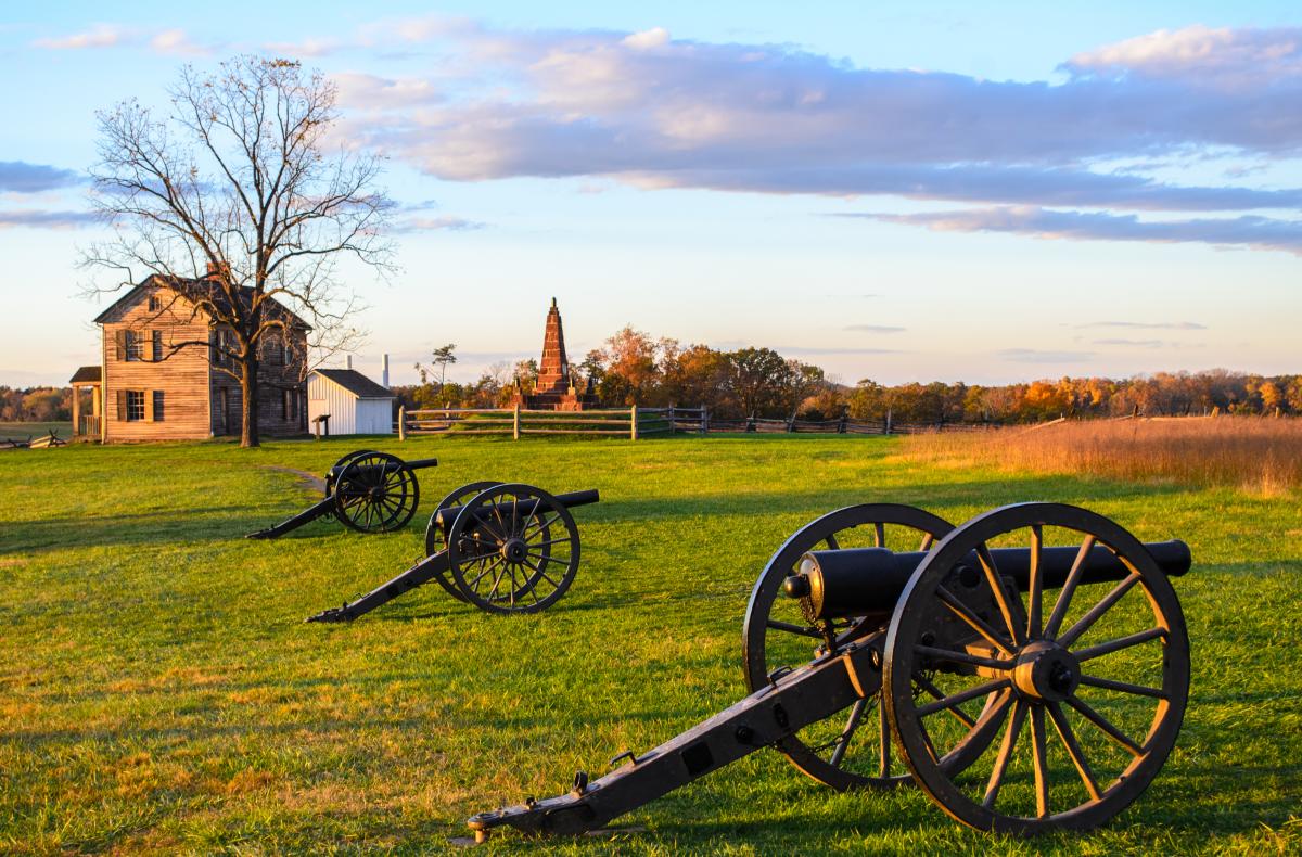 Three cannons on a battlefield with a historic house in the background