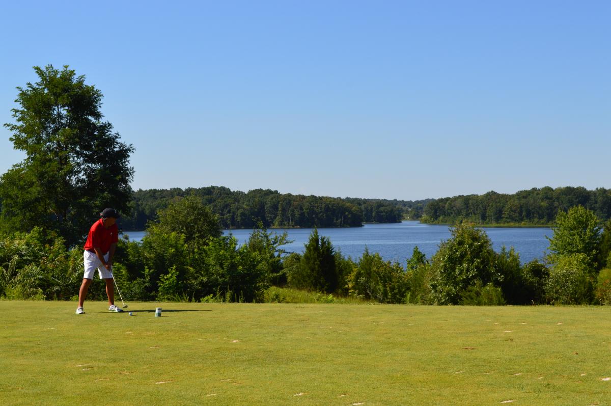 A man golfing on a golf course with a body of water in the background.