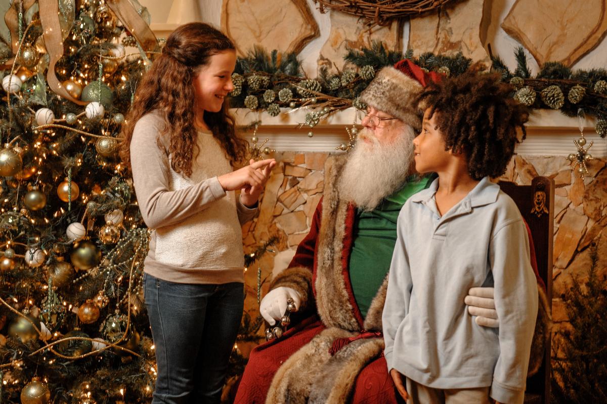 An old fashioned Santa Claus sits with one child on his lap and another standing talking to him during Kris Kringle’s Candlelight Christmas at Burritt on the Mountain