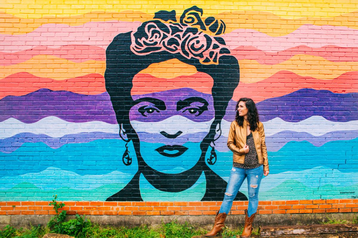 A visitor poses next to the Frida Mural on the Beaumont Mural Walk.