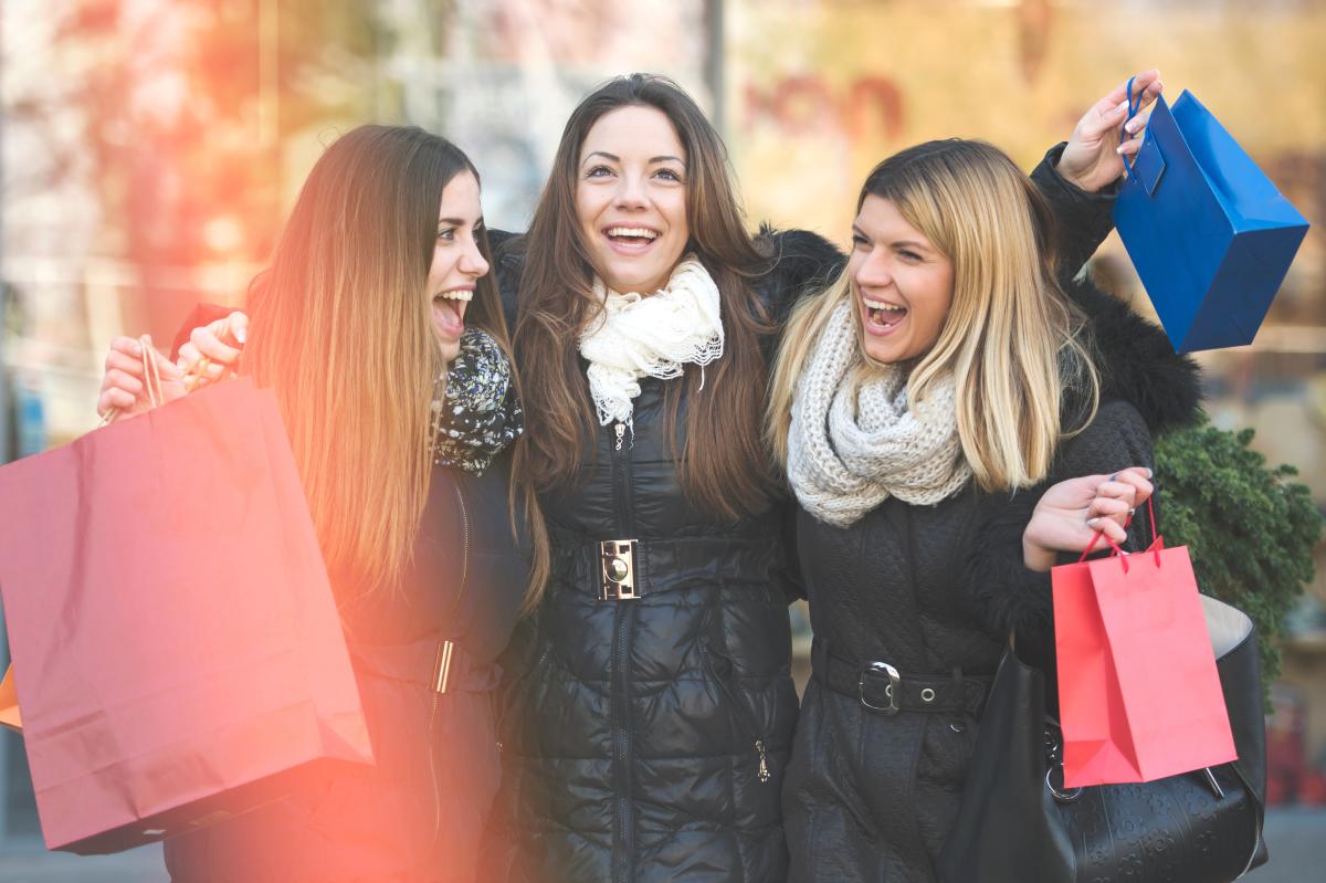 three girlfriends smiling and holding shopping bags