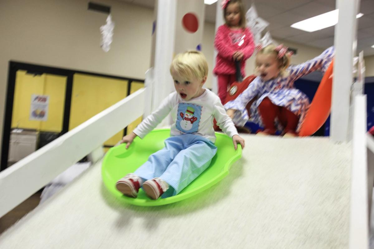 A young boy slides on a green toboggan on an indoor slide painted to look like it is snow-covered at Imagination Place
