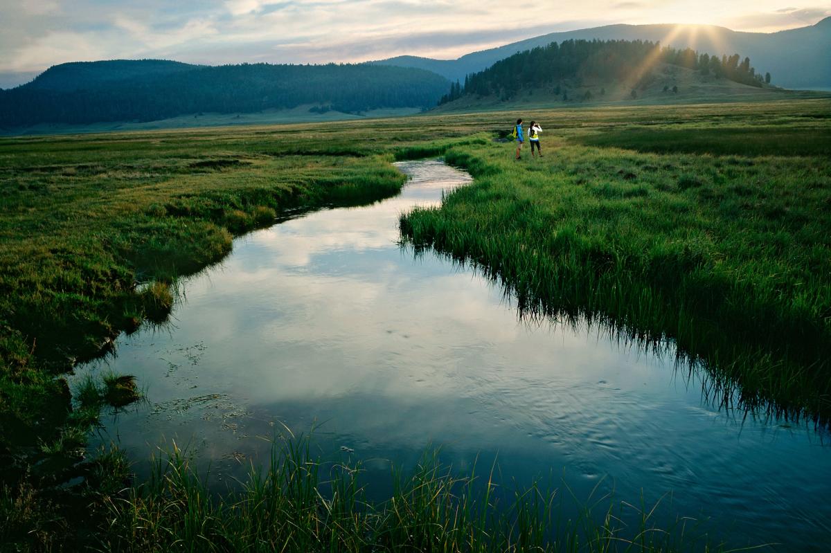 People walking along a creek in a grassy field at sunset at Valles Caldera in New Mexico
