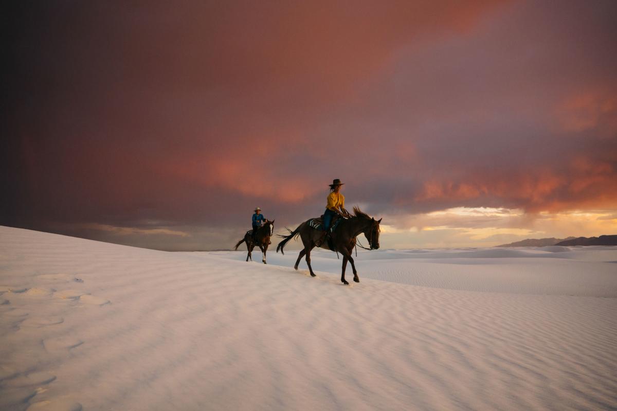 A couple rides horses at sunset at White Sands in New Mexico