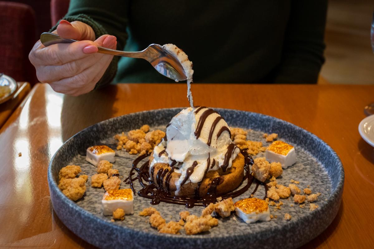 Chocolate Chip Cookie dessert topped with ice cream, chocolate drizzle, toasted marshmallows, and cookie crumble.
