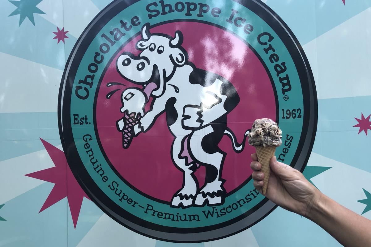 An individual holds an ice cream cone over a Chocolate Shoppe sign