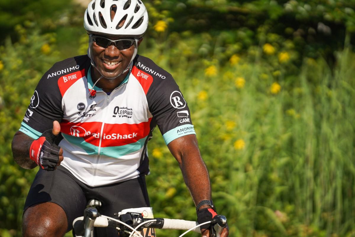 A male biker smiles and gives a thumbs up.