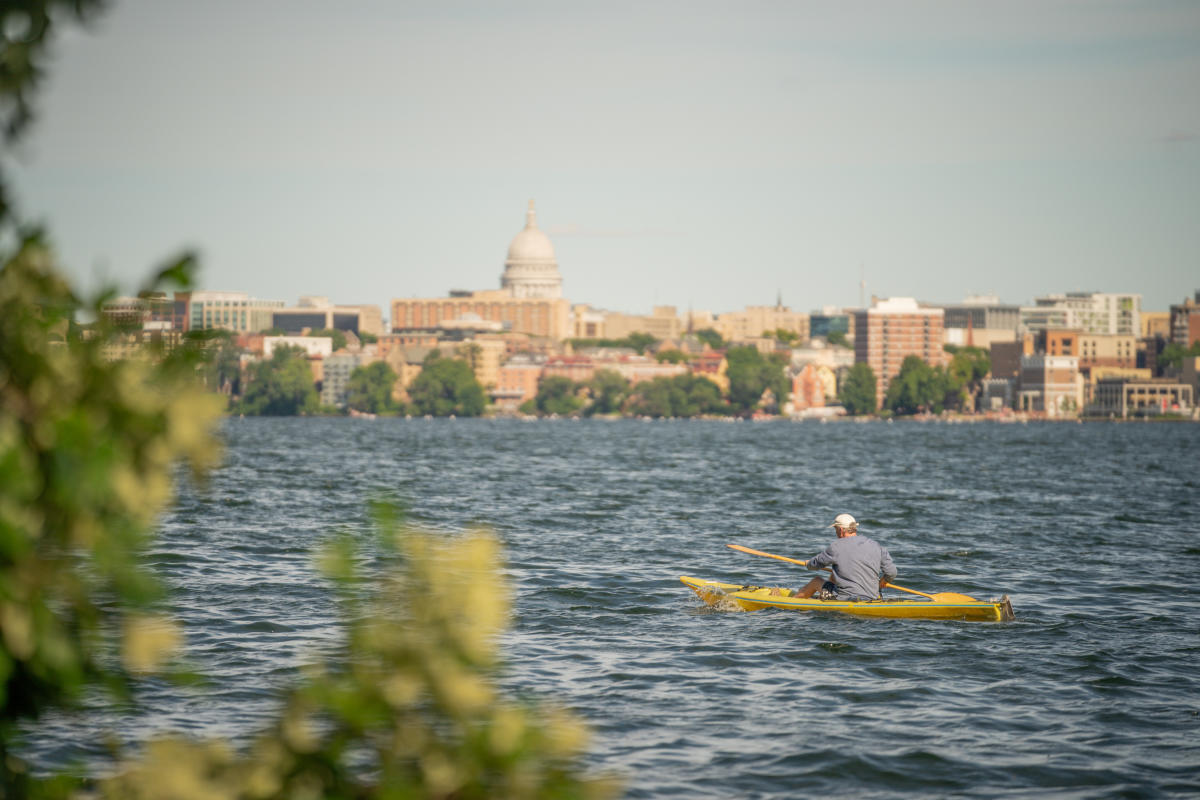 A man kayaks with the Madison skyline in the background