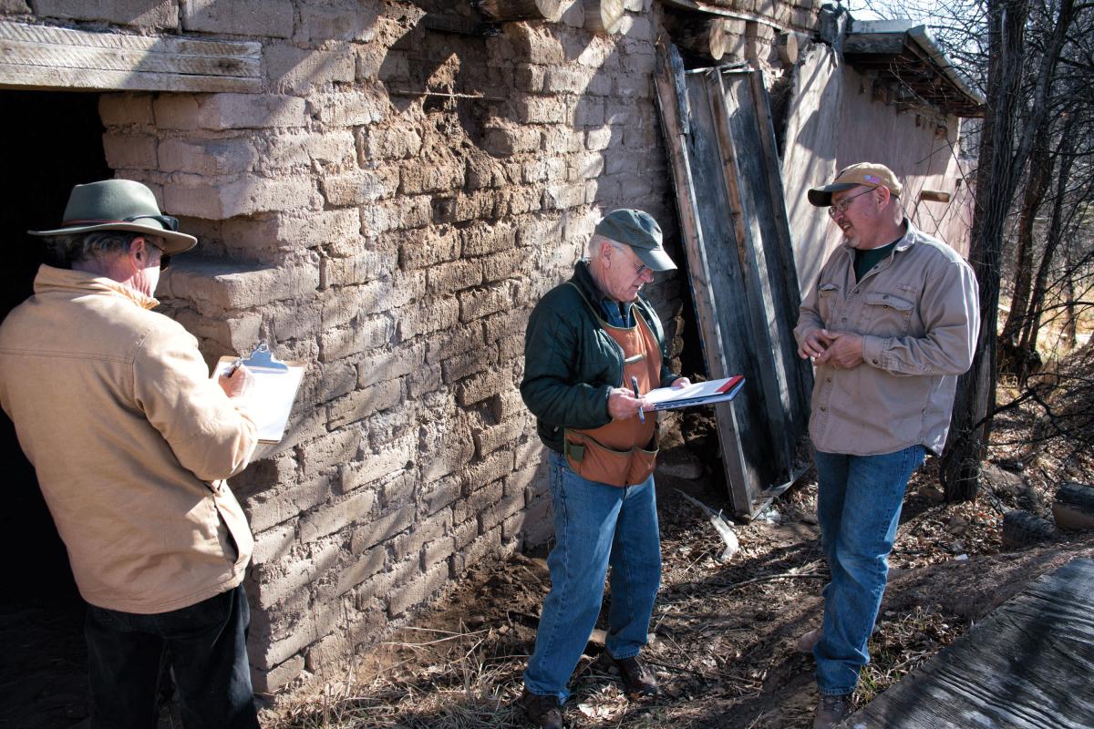 Adobe restorers consult their notes on how to shore up one of Casita Martina's walls.