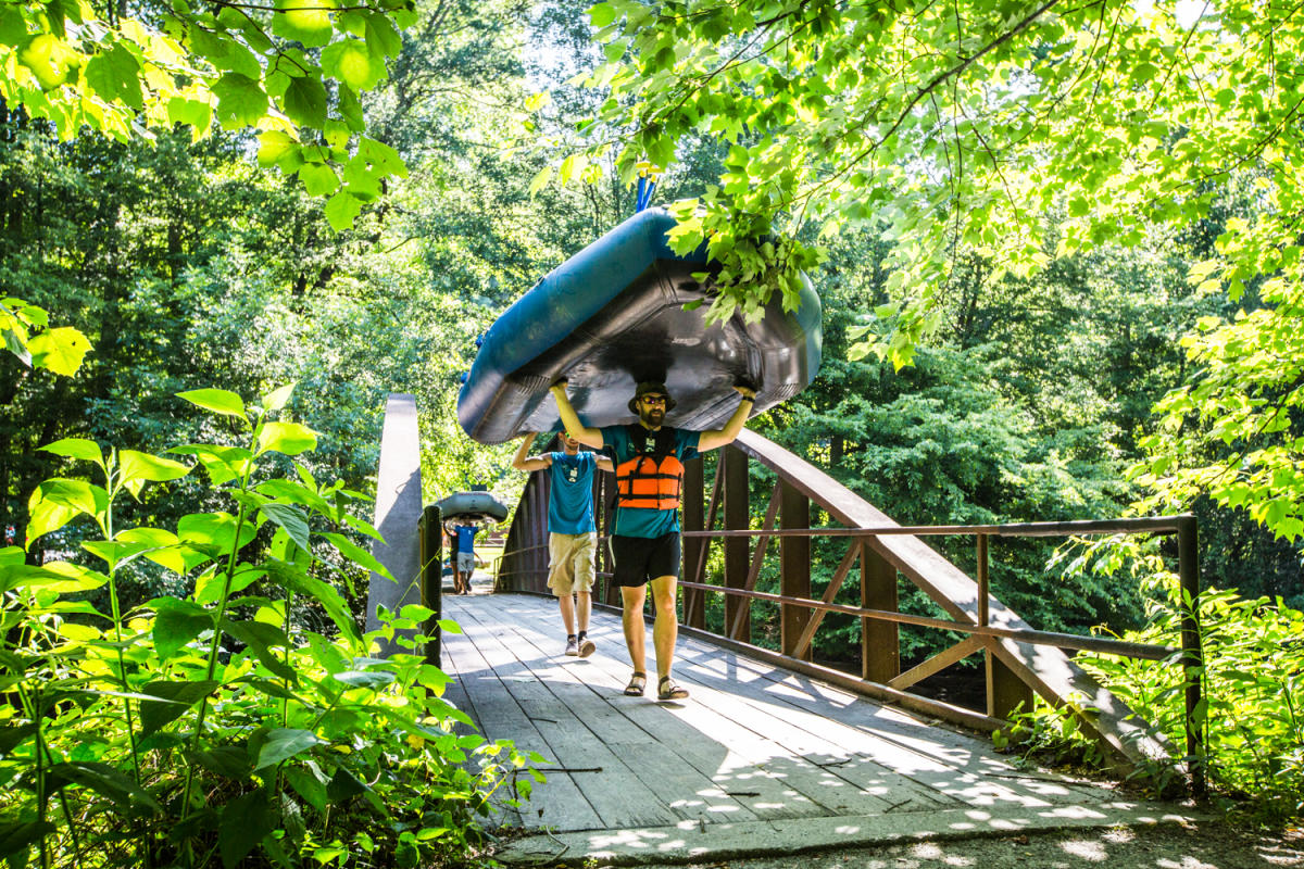 NOC River Guides carrying a boat above across a bridge.