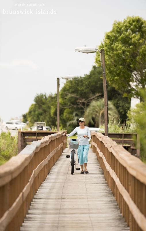 A woman walking her bike over a bridge in the Brunswick Islands, NC
