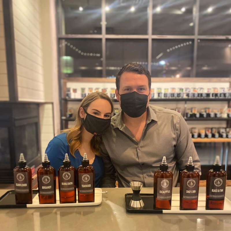 A couple wearing masks poses behind bottles of fragrances at Olfactory Scent Studio