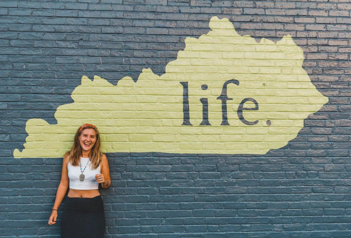 Laughing woman in front of a mural of Kentucky with the word 'life.' inside it.