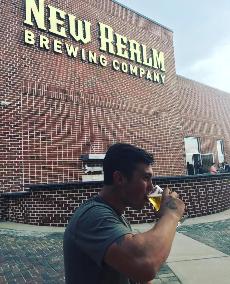 A patron sips a glass of brew in front of the New Realm Brewing signage.