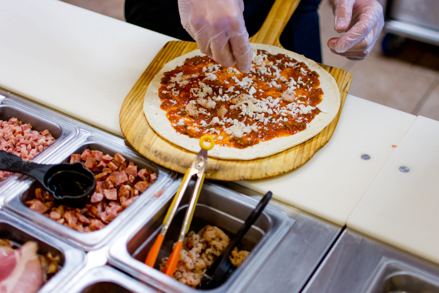 An employee making a fresh pizza at Pizza Artista in Lafayette, LA