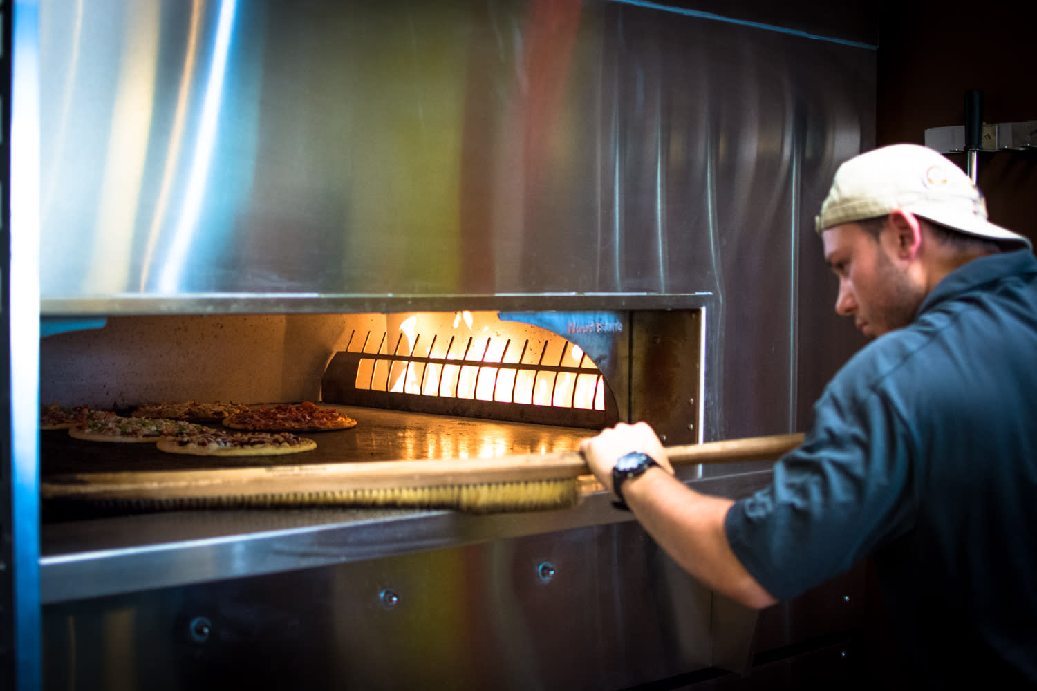 Employee making oven-fired pizzas at Pizza Artista in Lafayette, LA