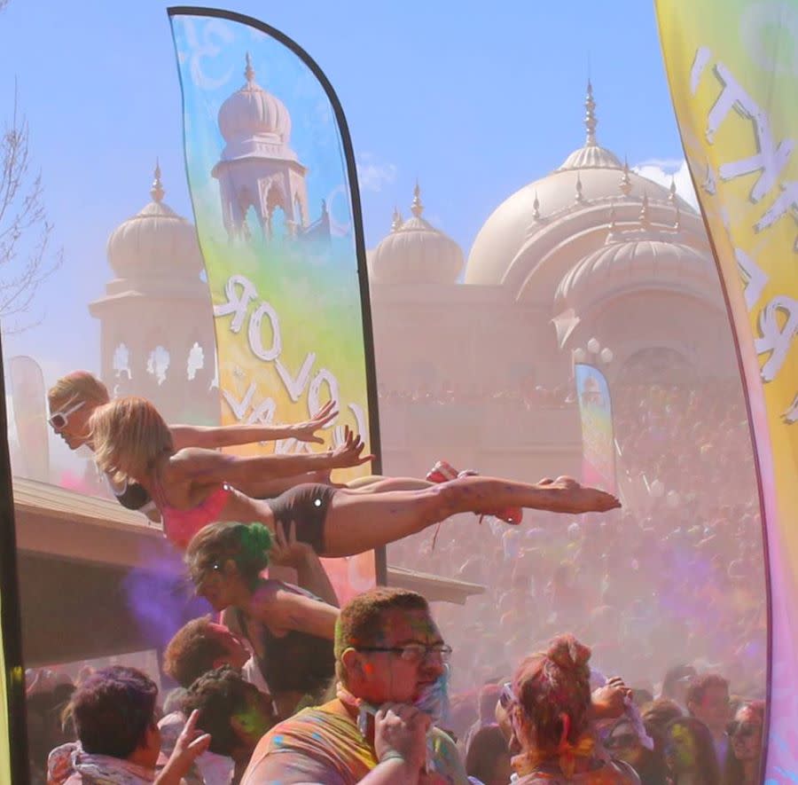 two people held in yoga positions above the crowd at Color Festival in front of temple