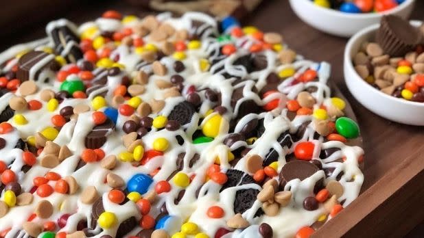 A chocolate pizza covered in oreos, m&ms and other candies topped with a white chocolate drizzle