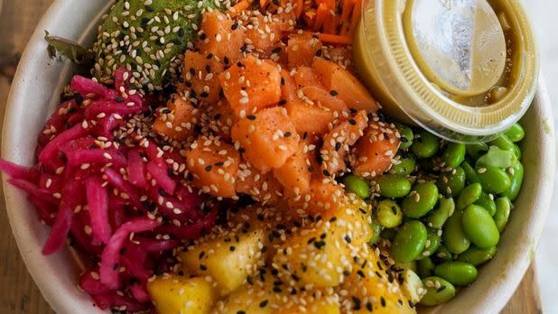 Colorful poke bowl, cubes of raw salmon, seaweed salad, pickled onions, edamame, sesame seeds