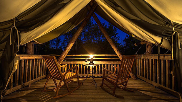 A glamping tent at night with a candle illuminating two rocking chairs