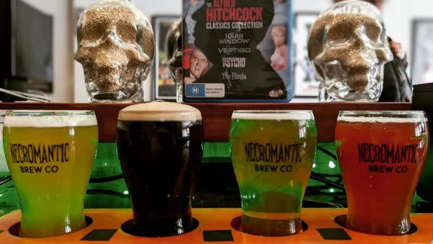 Four glasses of different colored beers in a row in front of eery decorative skulls