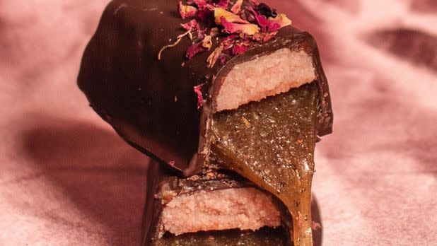 Artisan chocolate, topped with edible flowers, inside of chocolate shows a colored center layer and caramel layer