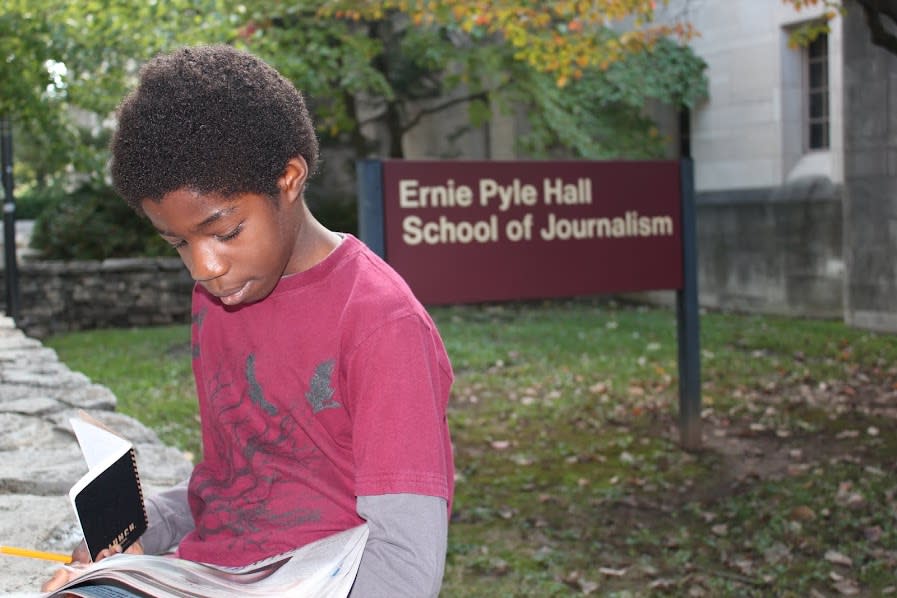Ben reads a newspaper in front of Ernie Pyle Hall School of Journalism